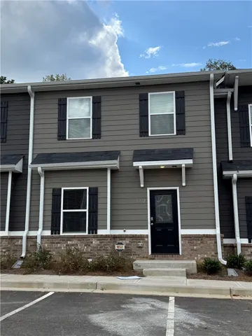 A contemporary townhome facade featuring gray siding, dark shutters, and brick accents awaits a new occupant.
