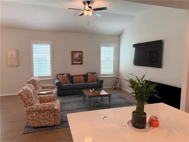 Generous living area featuring vaulted ceilings, a ceiling fan, and hardwood flooring.