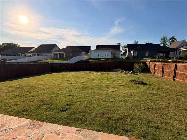 A spacious backyard with mature green grass, perfect for outdoor activities. Stained privacy fence with a 5' gate and a newly added oak tree.