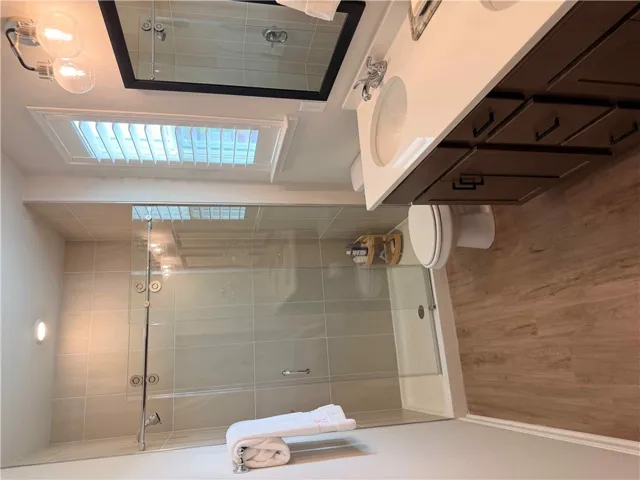 A well-lit bathroom with a glass-enclosed shower and wood LVP flooring, double vanity, plantation shutter treatments, and WI closet provides a serene retreat.