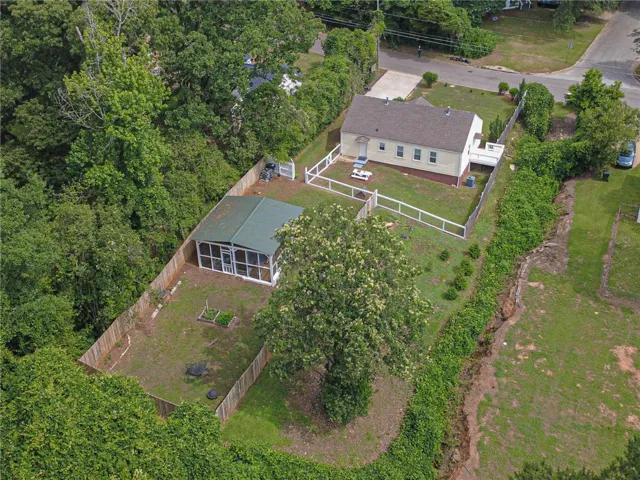 An aerial perspective reveals a cozy home, fenced yard, and a large outbuilding amidst verdant surroundings. Ample opportunities