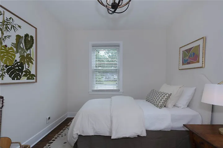 A well-lit bedroom features hardwood floors and a single window, creating a serene personal retreat.