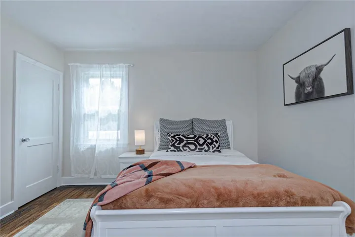Hardwood flooring grounds a cozy bedroom, featuring a window for natural light.