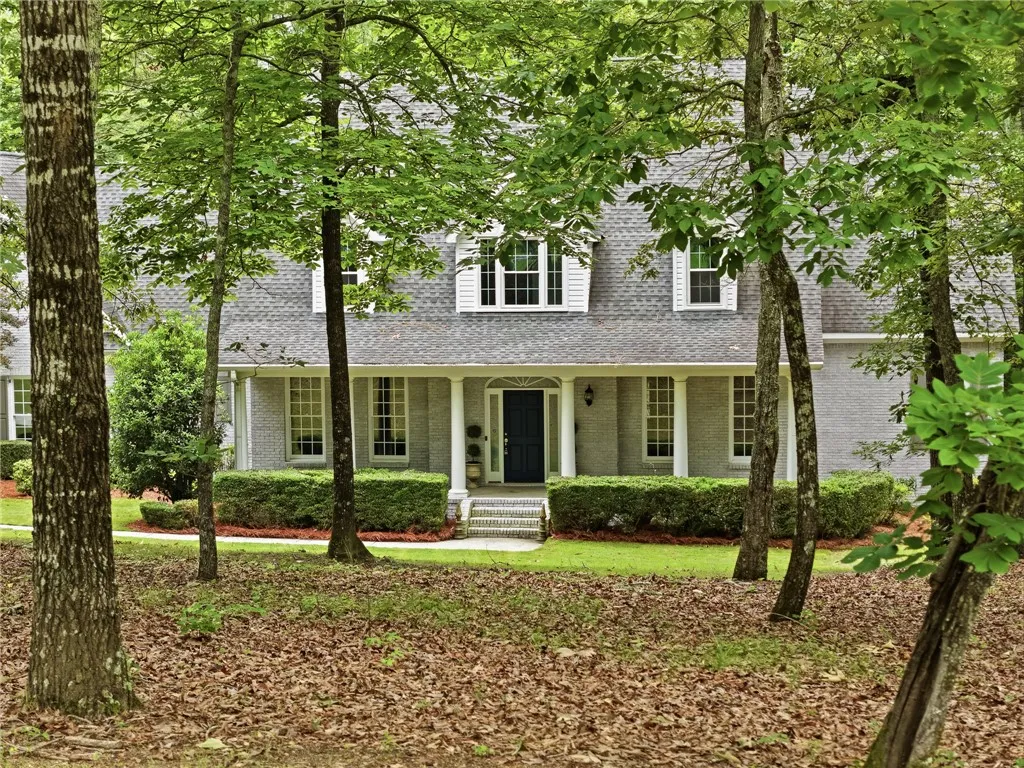 Mature trees frame a classic brick exterior complete with a welcoming columned front porch.