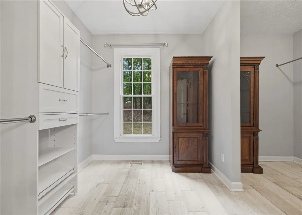A spacious dressing room features light-toned wood-look flooring and custom built-in cabinetry.
