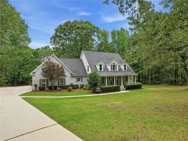 Mature trees frame a classic brick and siding exterior featuring dormer windows and a front porch.