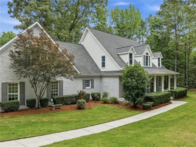 Mature trees and neat landscaping frame a stately traditional facade with a welcoming front porch.