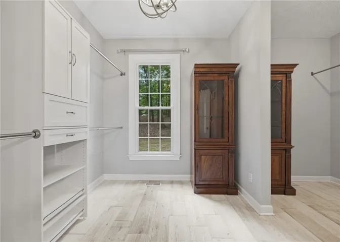 A spacious dressing room features light-toned wood-look flooring and custom built-in cabinetry.