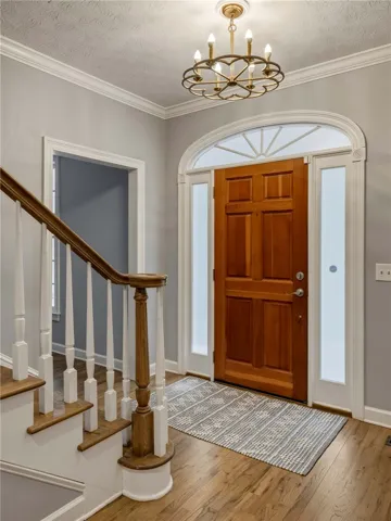 An inviting entryway showcases polished hardwood flooring and a classic wooden door under crown molding.