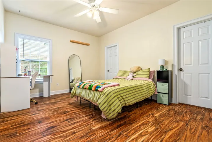 Rich hardwood-style flooring extends across this naturally illuminated bedroom, offering a warm and inviting atmosphere.