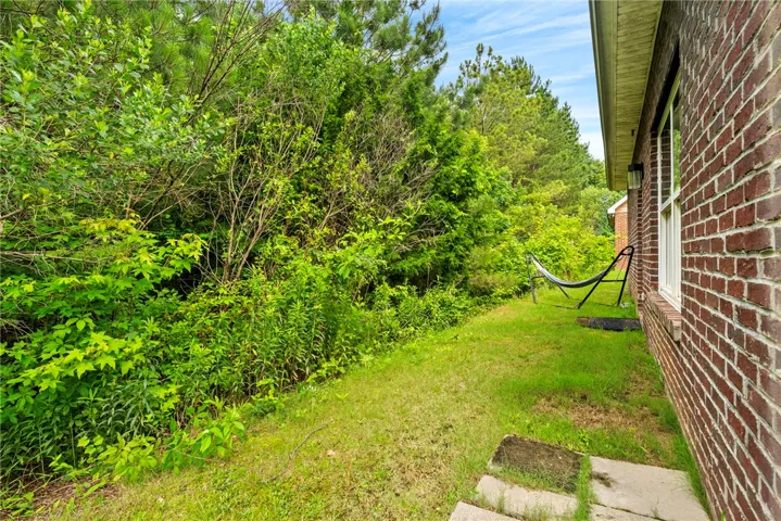 A tranquil side yard features verdant foliage, a brick exterior, and a ready hammock.