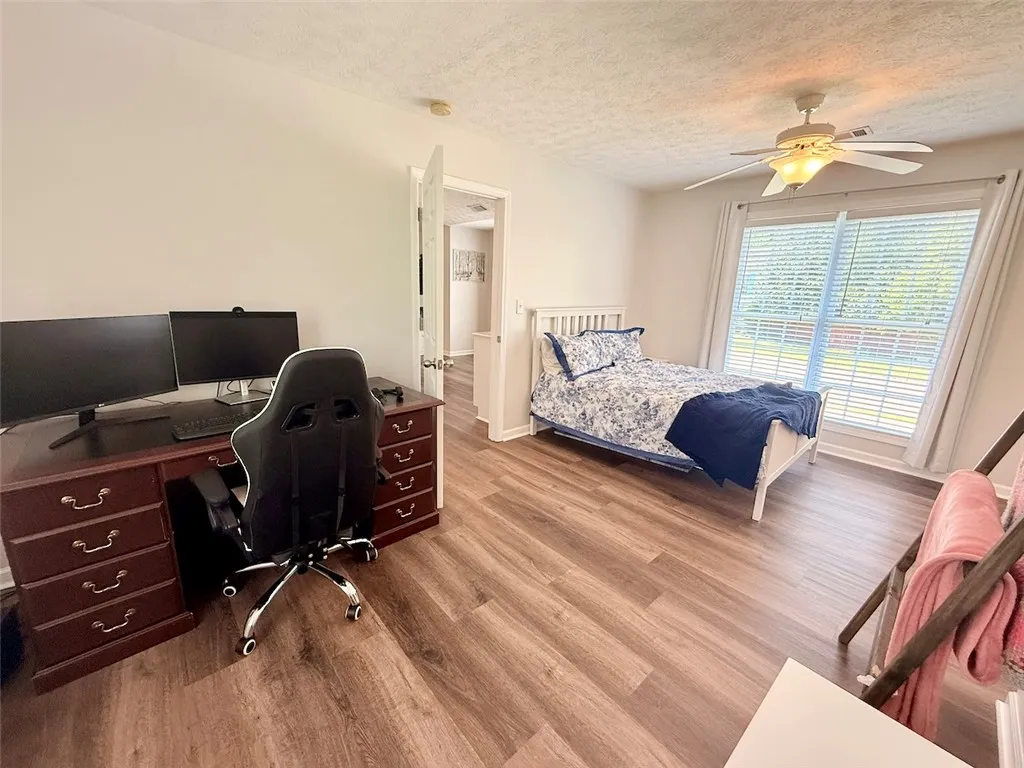 Well-lit room featuring durable laminate flooring, a refreshing ceiling fan, and large windows with privacy blinds.