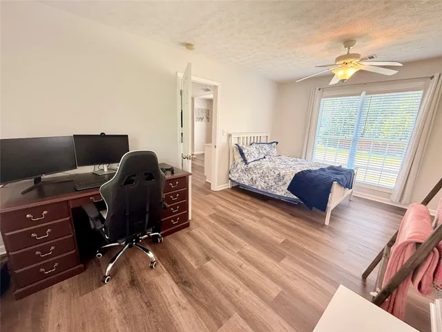 Well-lit room featuring durable laminate flooring, a refreshing ceiling fan, and large windows with privacy blinds.