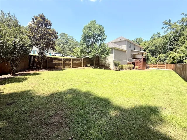 A spacious, enclosed backyard offers ample green space and privacy with mature trees and a fenced perimeter.