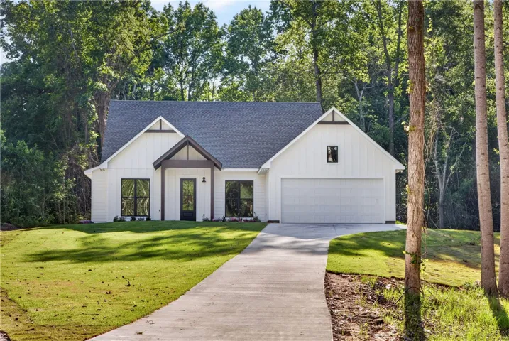 A graceful white farmhouse-style home is framed by verdant trees, offering a private retreat.