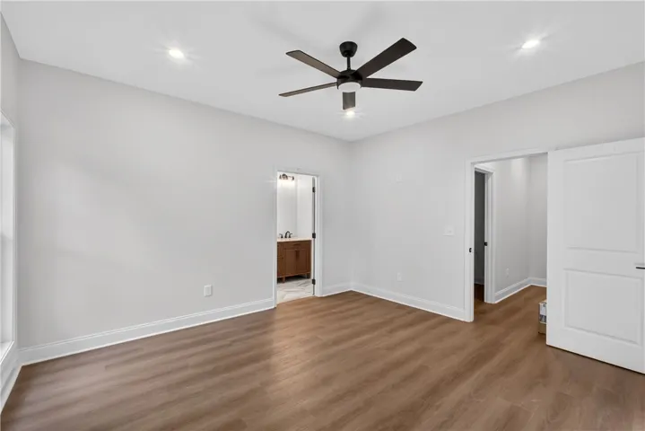 A spacious room awaits personalization, featuring rich hardwood-style flooring and a contemporary ceiling fan.