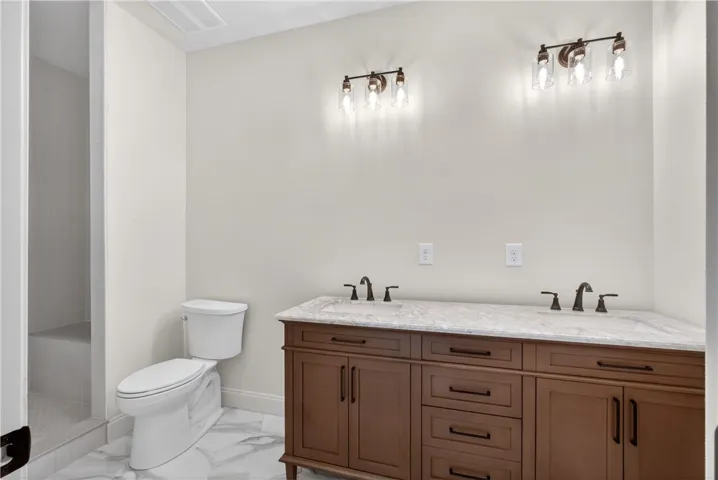 Marble-look tile flooring flows into a spacious shower, complementing the warm wood vanity and dual sinks.