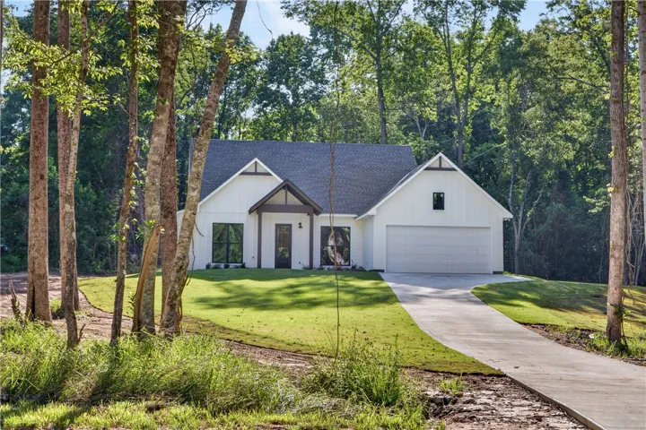 A newly constructed modern farmhouse with a pristine lawn, inviting entry, and an attached garage.