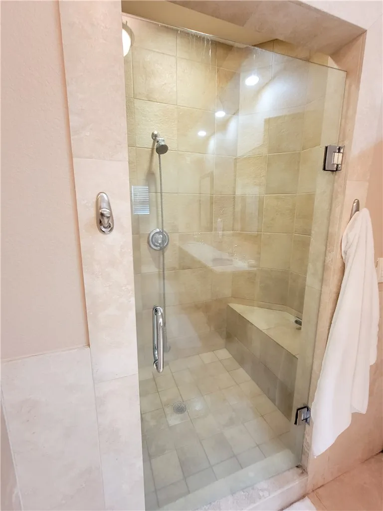 A well-lit, tiled shower enclosure with a built-in bench and glass door provides a refreshing bathing experience.