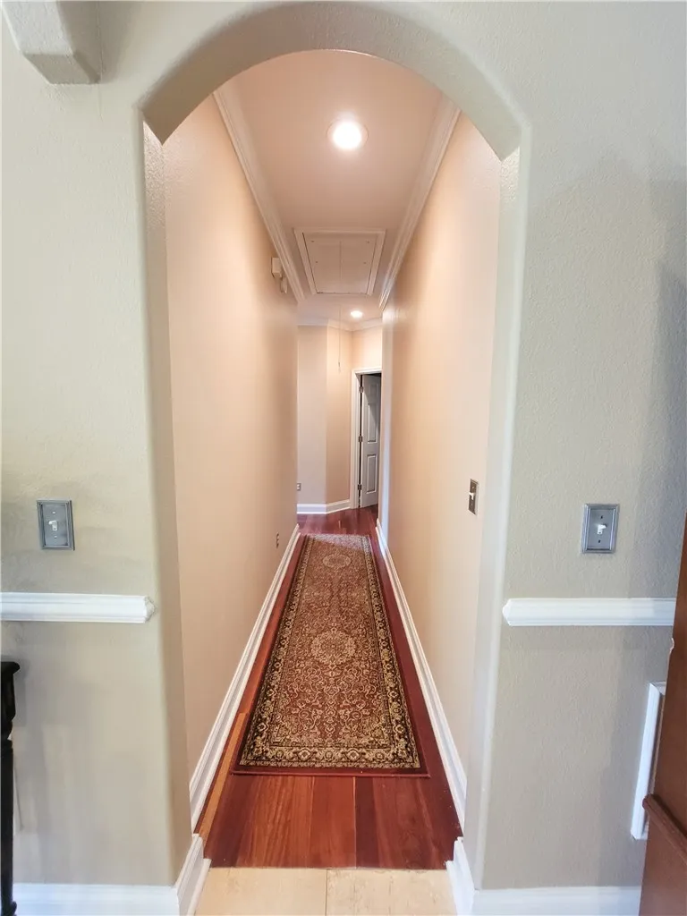 An inviting arched entryway frames a long, well-lit hallway with rich wood flooring.
