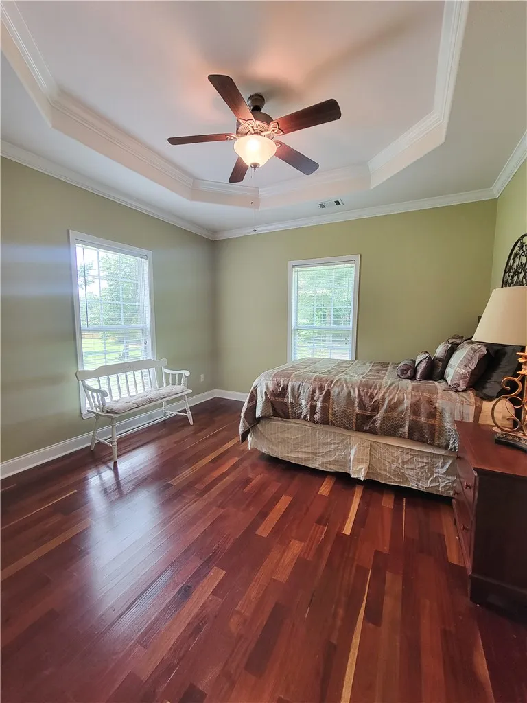 Rich hardwood floors complement a bedroom adorned with crown molding and a practical ceiling fan.