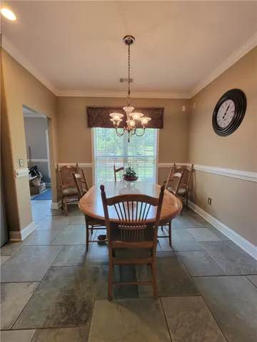 A classic chandelier illuminates this dining room featuring rich, natural-toned flooring and crisp crown molding.