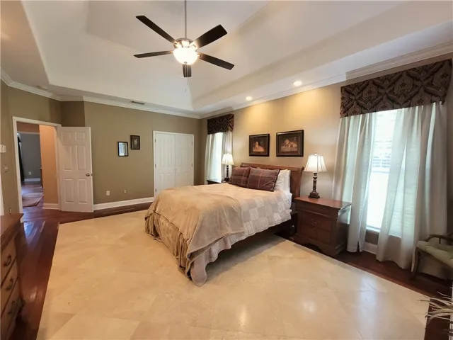 Recessed lighting and a ceiling fan illuminate this spacious primary bedroom featuring tray ceilings and two closets.