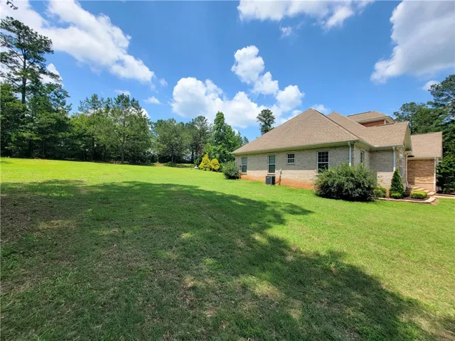 A spacious yard stretches beside a charming brick home, backed by a lush tree line.
