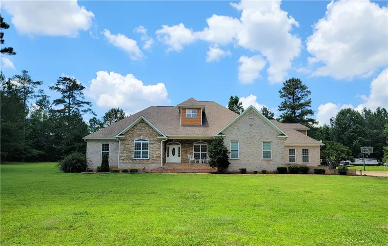 A spacious home with stone and brick accents boasts a wide front lawn and mature trees.