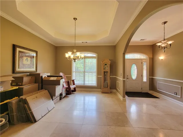 Ornate chandeliers illuminate a spacious interior with elegant tray ceilings and tile flooring.