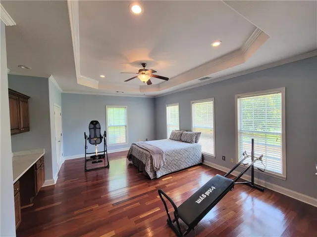 Rich hardwood floors complement the elegant tray ceiling and ample natural light in this spacious bedroom.