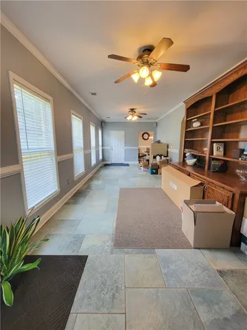A lengthy living area showcases built-in shelving, tile flooring, and multiple windows.