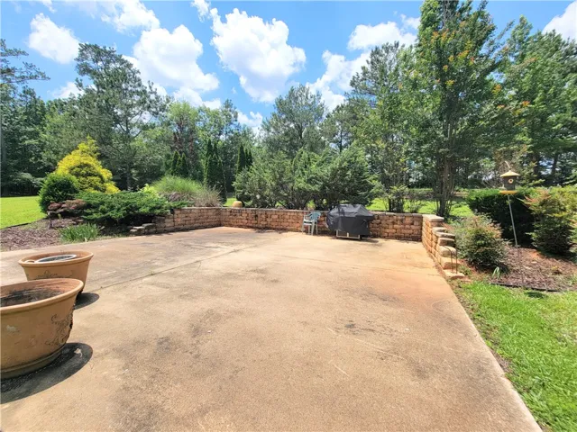 A spacious patio area bordered by a low stone wall and lush green landscaping invites outdoor living.