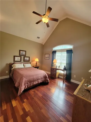 Elegant hardwood flooring grounds this bedroom, complemented by a vaulted ceiling and functional ceiling fan.