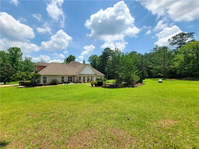A spacious lawn unfolds before a classic home, framed by lush trees under an expansive sky.