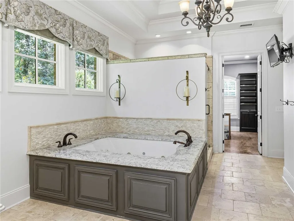 Crown molding and tiled floors frame a deeply recessed soaking tub beneath high ceilings.
