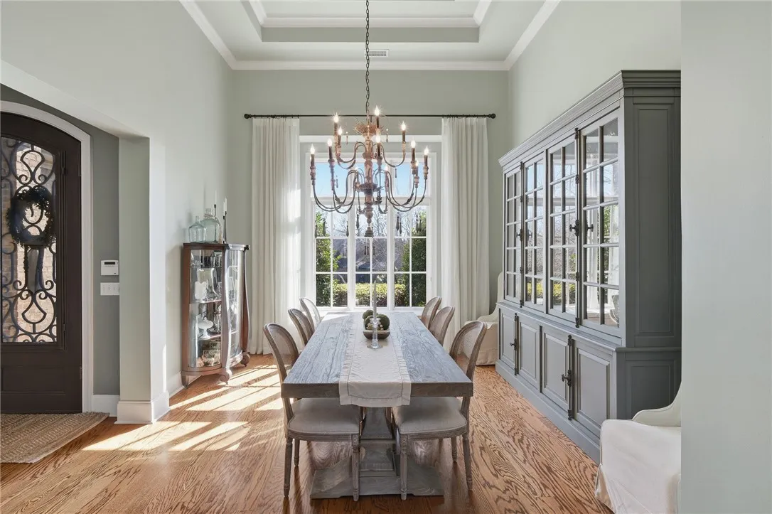 Natural light illuminates the rich hardwood floors and elegant tray ceiling in this spacious dining area.