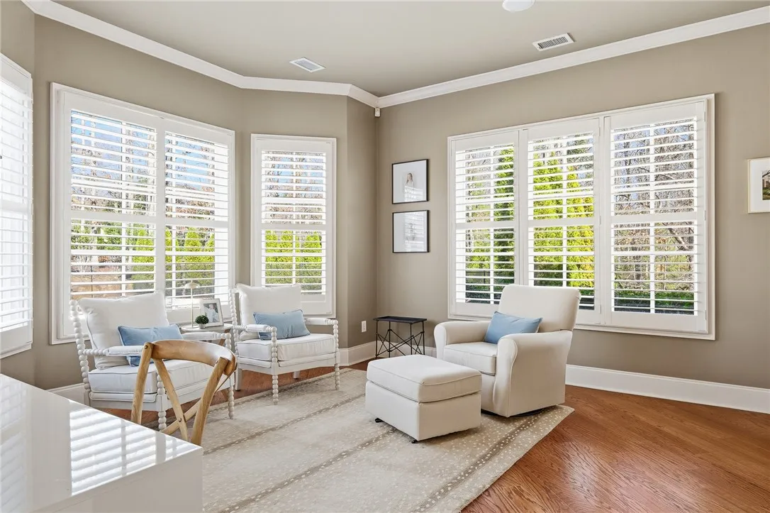 Sun-filled room boasts hardwood floors and multiple large windows with elegant white shutters.