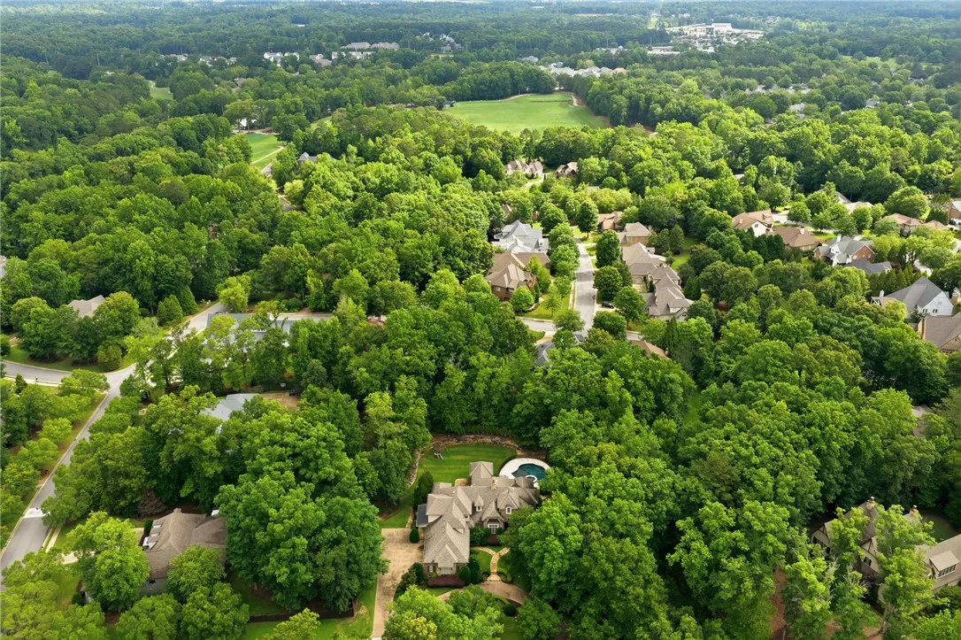 An aerial perspective showcases a private pool and ample green space within a verdant neighborhood setting.
