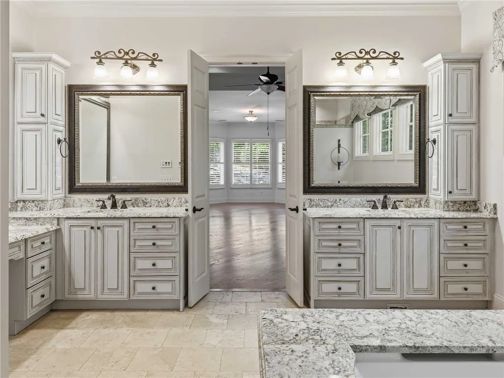 Ornate dual vanities with granite counters frame the entrance to a bright bedroom suite.