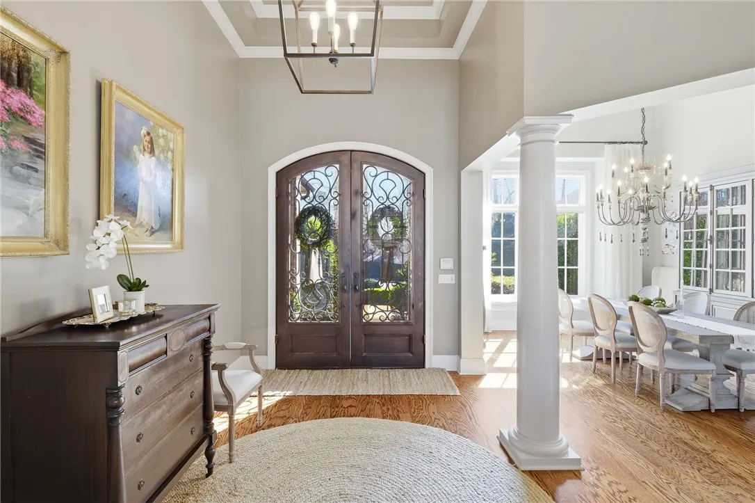 Ornate double doors welcome you into a grand foyer featuring gleaming hardwood floors and an elegant dining area.