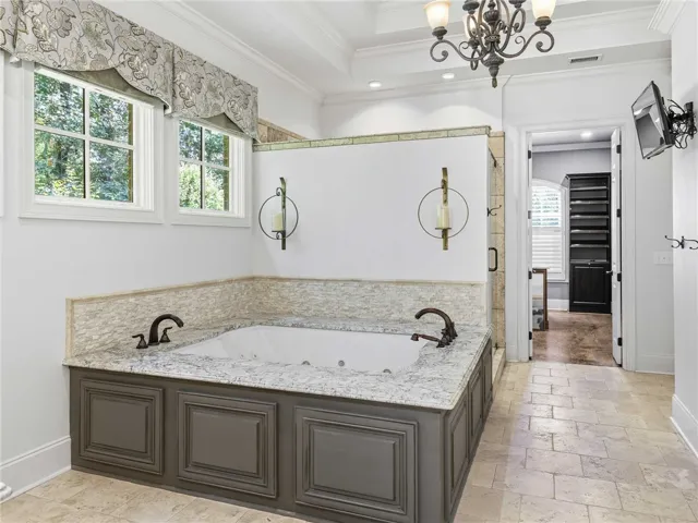 Crown molding and tiled floors frame a deeply recessed soaking tub beneath high ceilings.