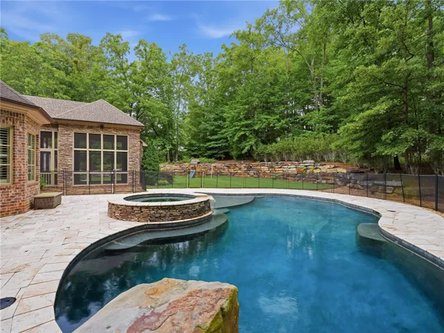 An inviting backyard oasis with a pristine pool and spa, set against a backdrop of mature trees.