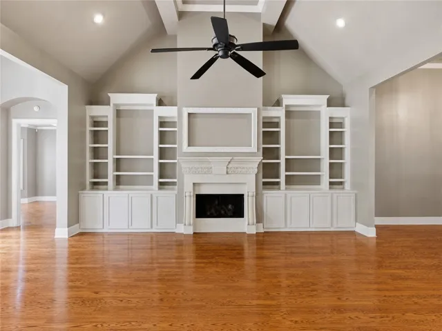 A spacious great room featuring high vaulted ceilings, a prominent fireplace, and rich hardwood flooring.