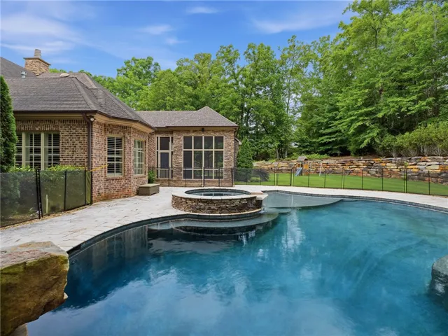 Backyard oasis with a sparkling pool and spa, framed by lush mature trees and a brick-and-stone residence.