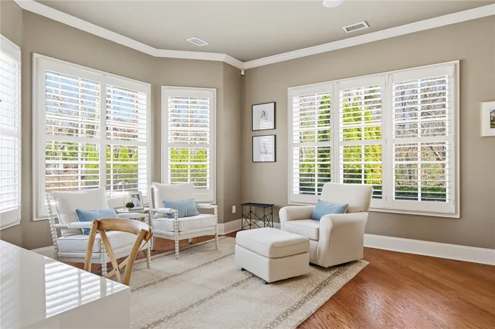Sun-filled room boasts hardwood floors and multiple large windows with elegant white shutters.