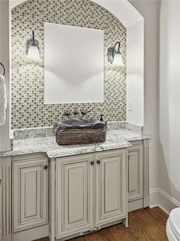 An elegant stone vanity rests beneath a mosaic-tiled arched alcove with wall-mounted lighting.
