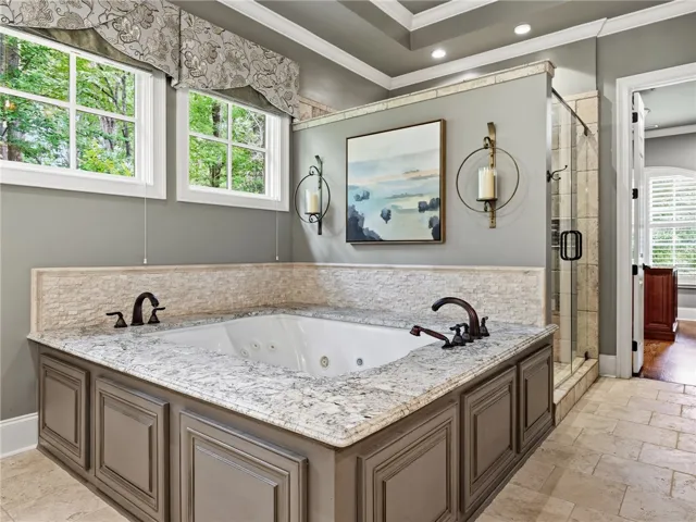 An inviting soaking tub with stone counters and decorative wall sconces defines this relaxing bathing space.