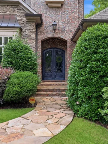 An inviting stone pathway leads to a grand arched entry with ornate wrought-iron doors.