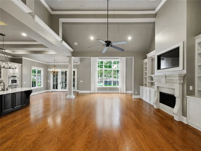 Natural light illuminates rich hardwood floors in this spacious living area with soaring ceilings and a grand fireplace.